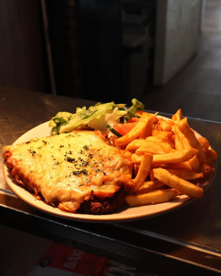 Featured image for “Craving a classic? Our Chicken Parmy is a crowd favourite  crispy schnitzel topped with rich sauce and melted cheese, served with chips and salad.”